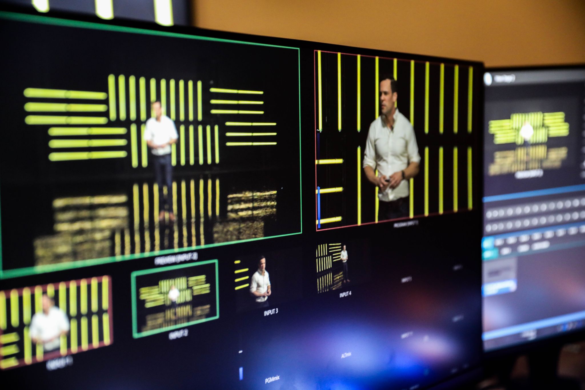 Live production monitor wall showing multi-camera feeds of a speaker on stage